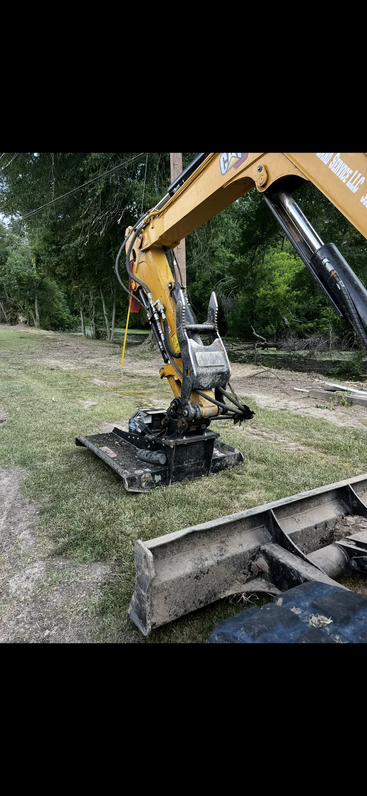 Yellow compact excavator with bucket on cleared lot, concrete blocks and grading equipment visible