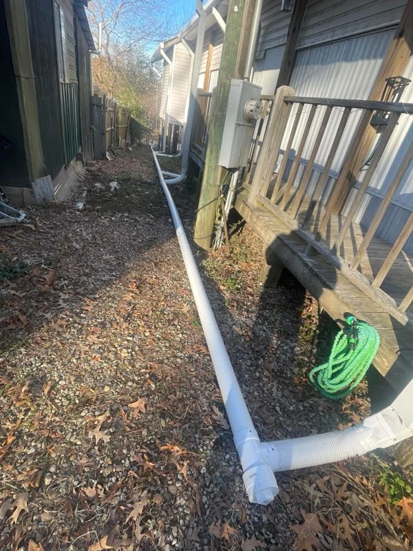 White PVC drainage pipe installed in trench with landscape fabric and mulch along residential property
