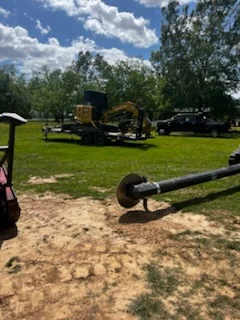 Tracked excavator and heavy equipment on cleared grass lot with debris pile