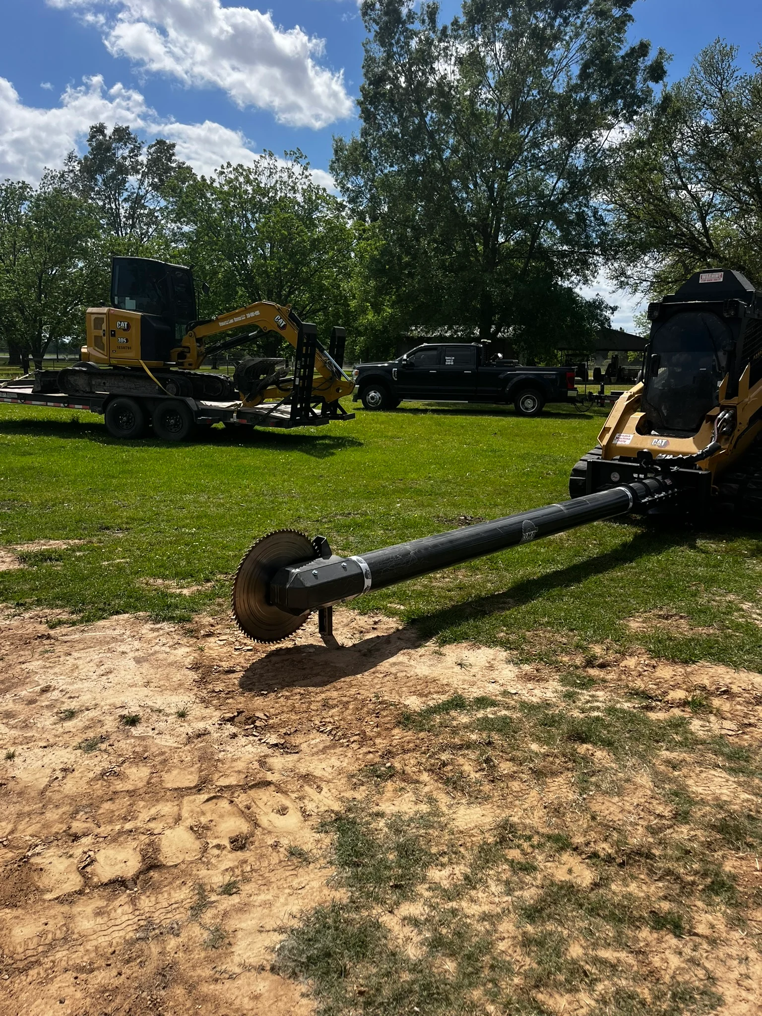 CAT skid steer and excavator equipment fleet on grass with trailer transport