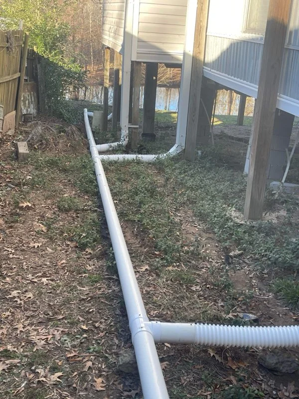 White PVC and corrugated drainage pipe installation under residential structure with wooden support posts