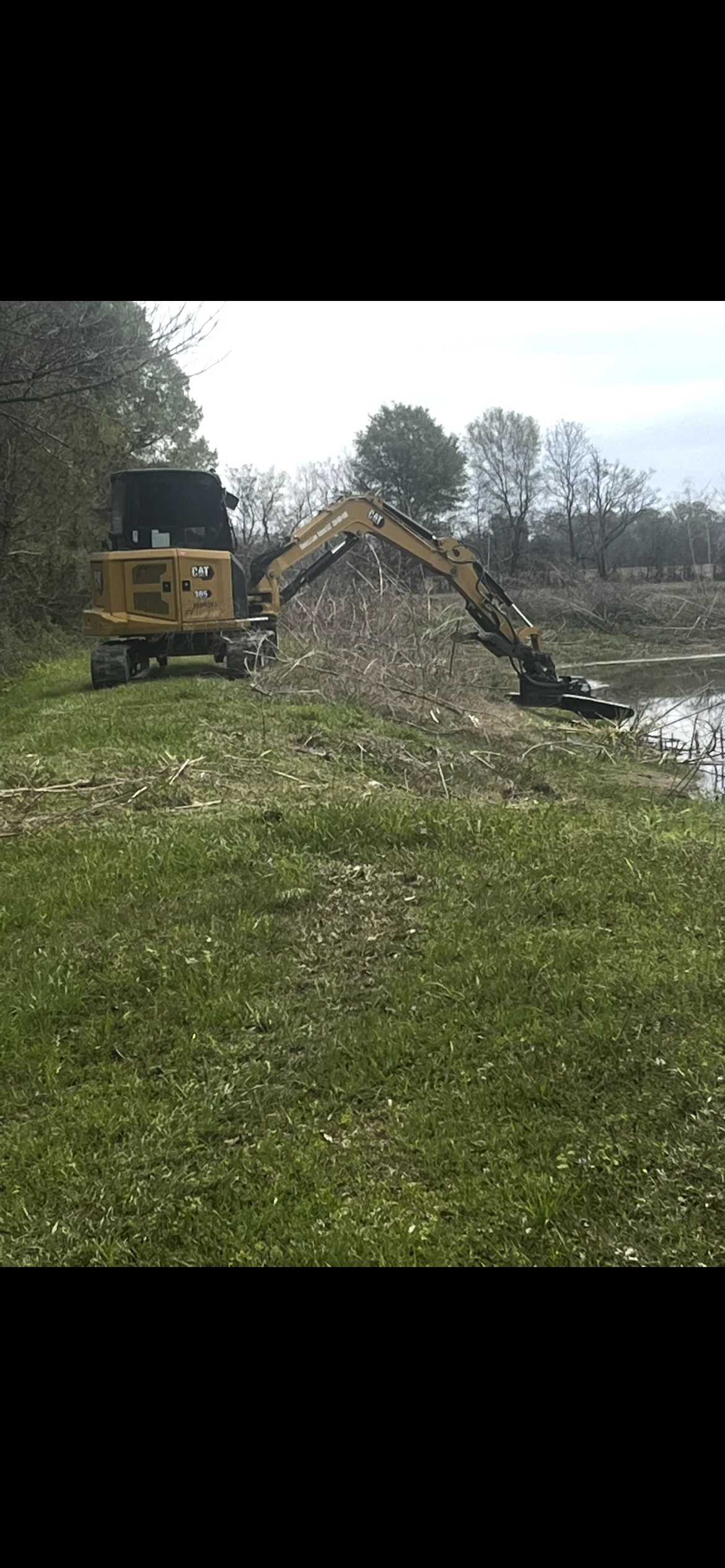 CAT excavator with grapple bucket clearing fallen trees and brush from waterfront property