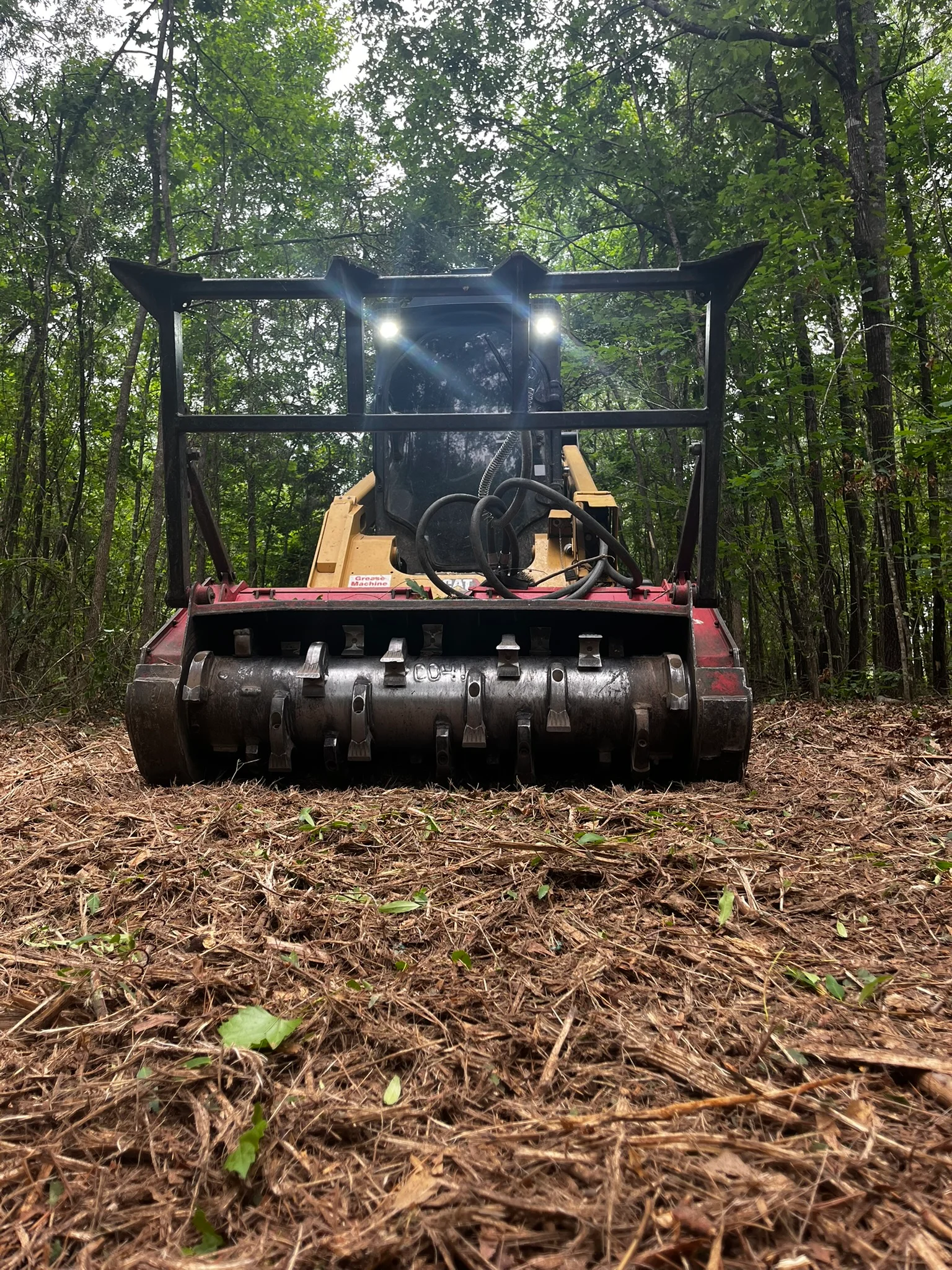 Tracked mulcher with black cab and red frame clearing wooded land, industrial mulching drum visible