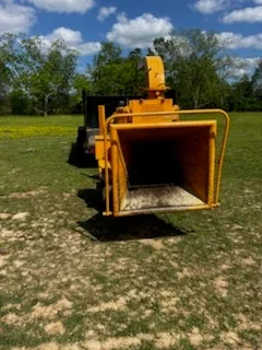Yellow industrial wood chipper with open hopper on cleared land