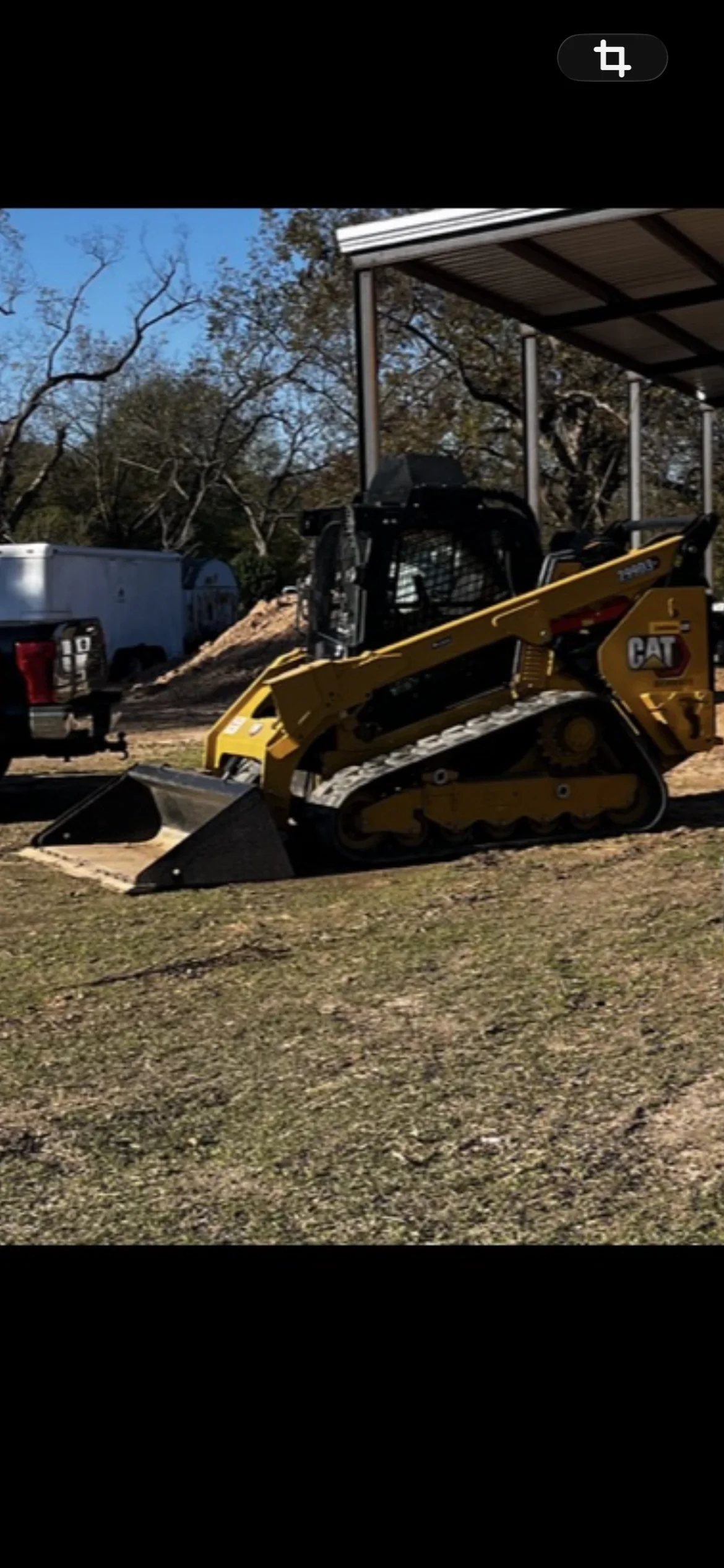 CAT track loader clearing and grading dirt site with metal carport structure
