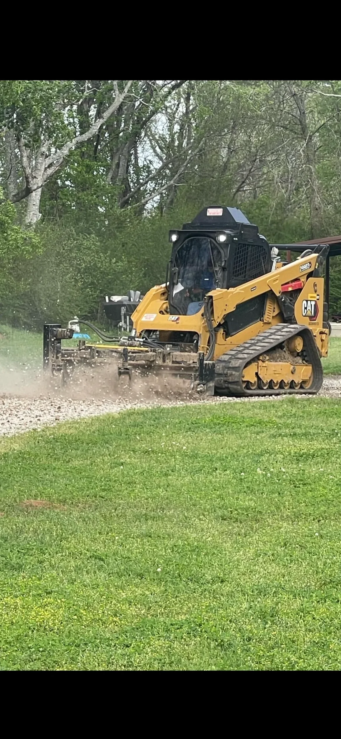 CAT skid steer with grader blade compacting gravel driveway surface