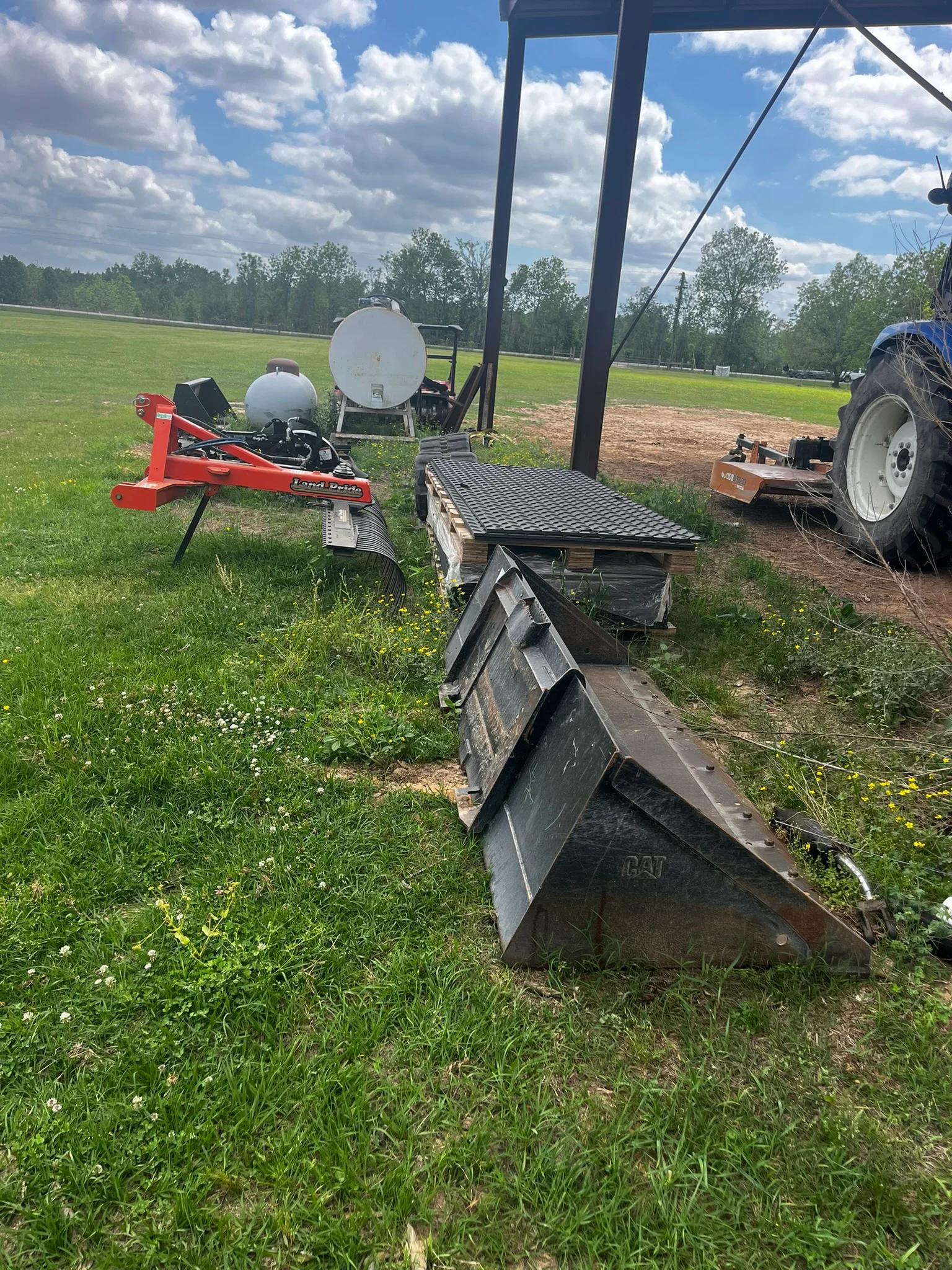 CAT loader bucket, red log splitter, water tanks, and metal platform on cleared agricultural site