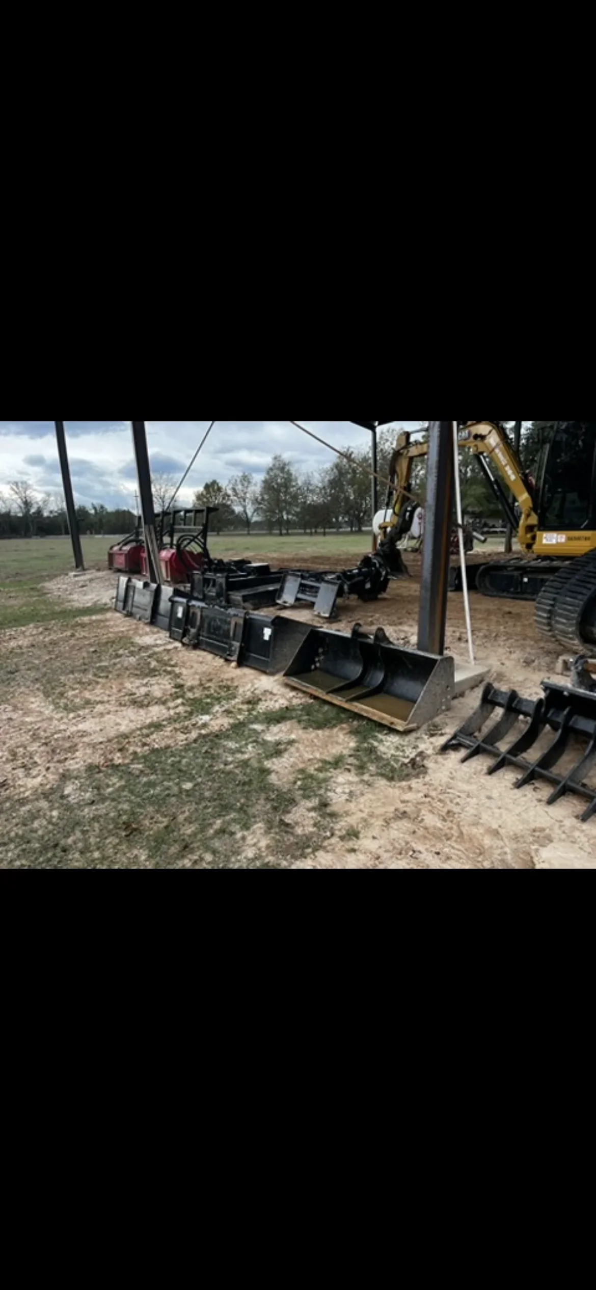 Excavation equipment and buckets staged under canopy with excavator on prepared ground