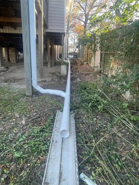 White PVC drainage pipe installed under residential structure with proper grading