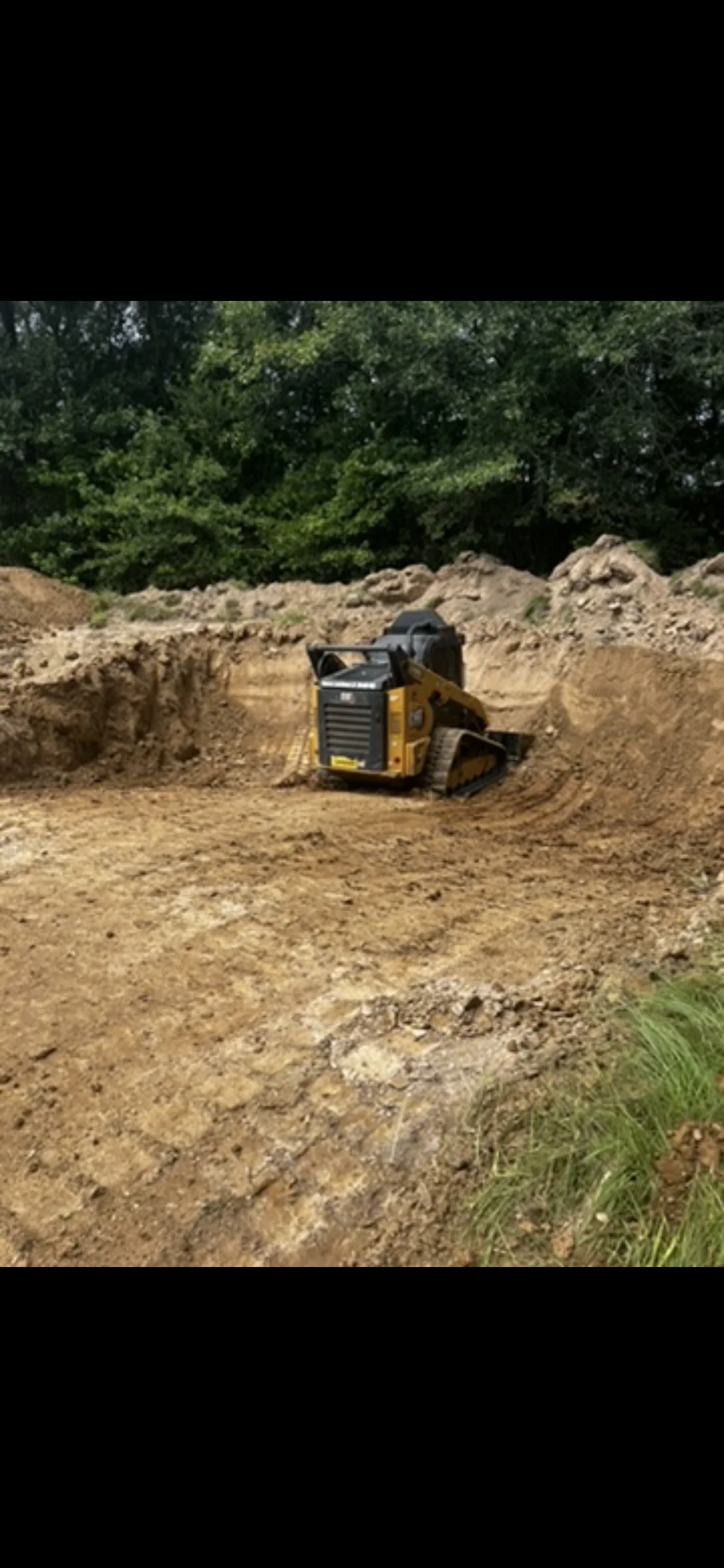 Yellow skid steer loader grading soil and earth material on cleared construction site
